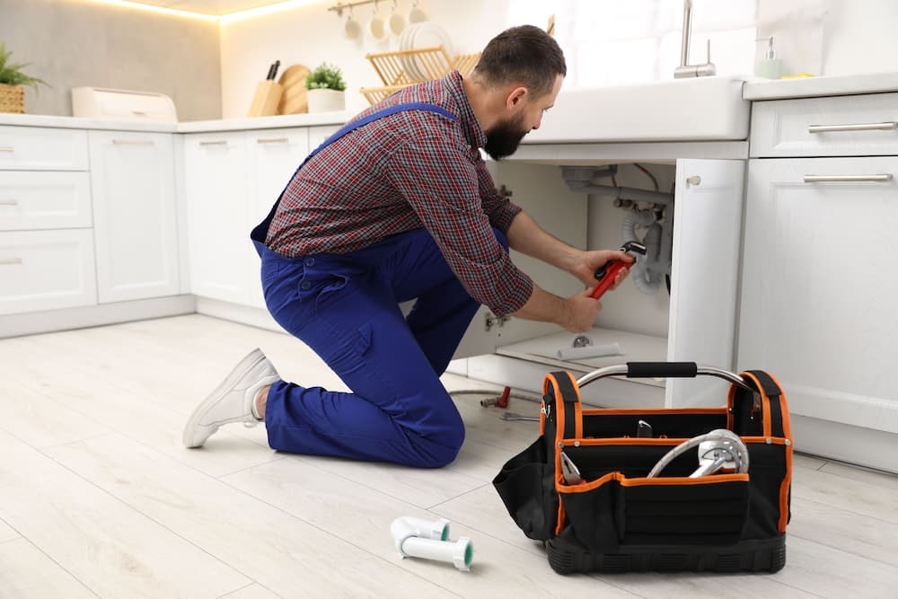 Plumber working on sink plumbing in bright kitchen