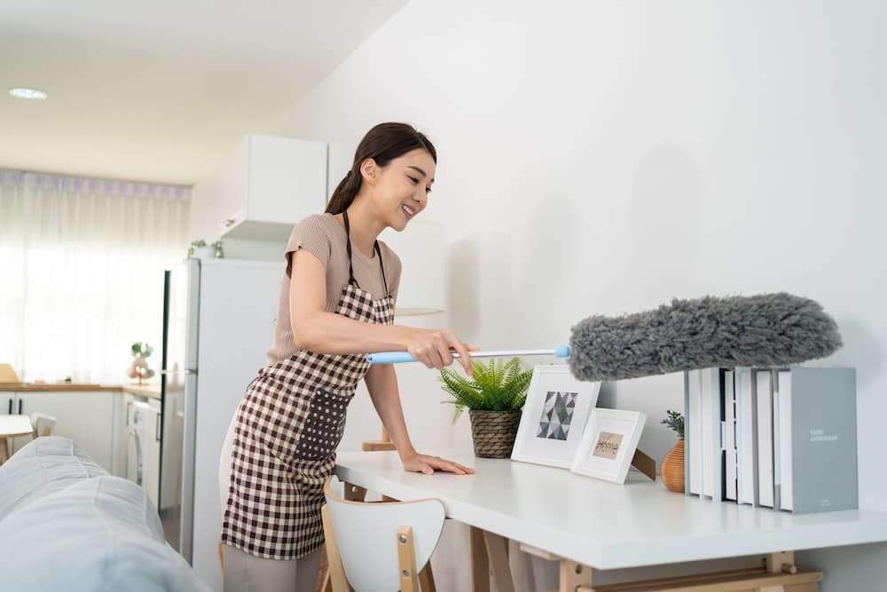 Woman dusting furniture in bright airy home
