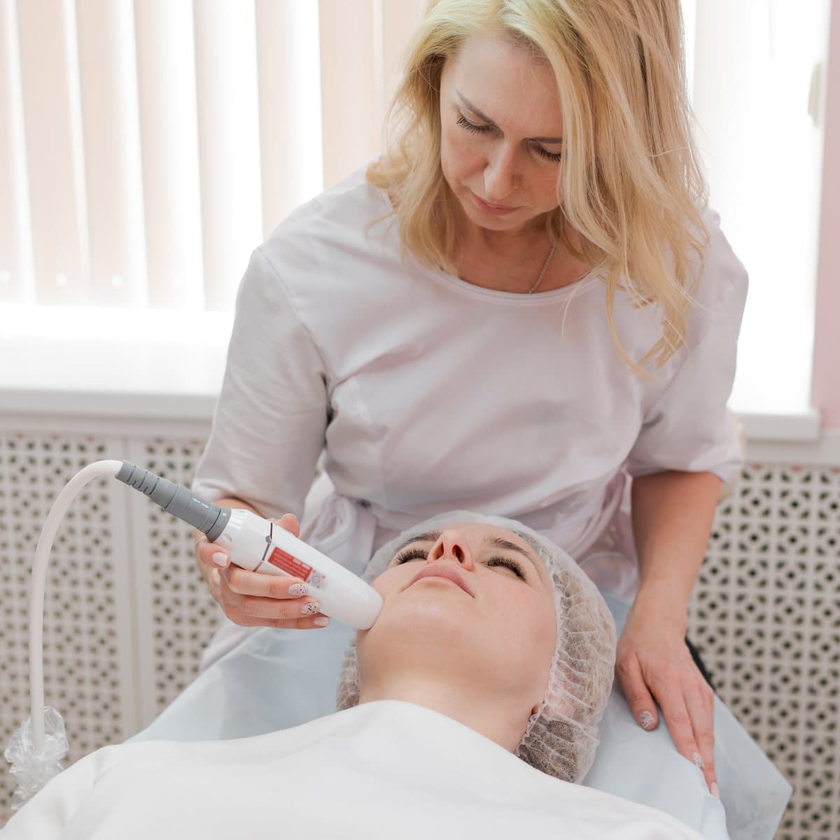 A practitioner delivering a device-led facial treatment in a clinic.
