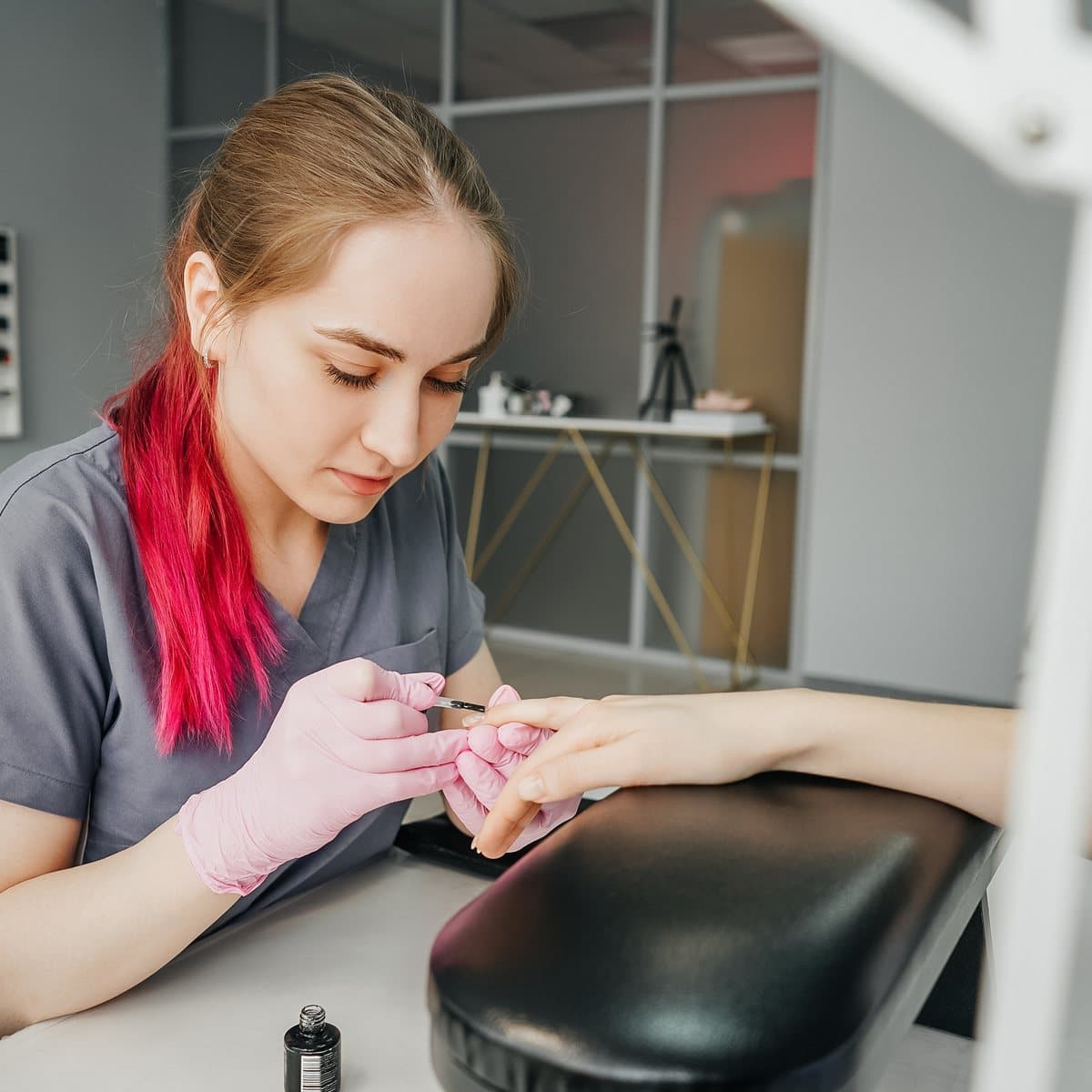 A nail technician working on a client’s manicure at a nail desk.