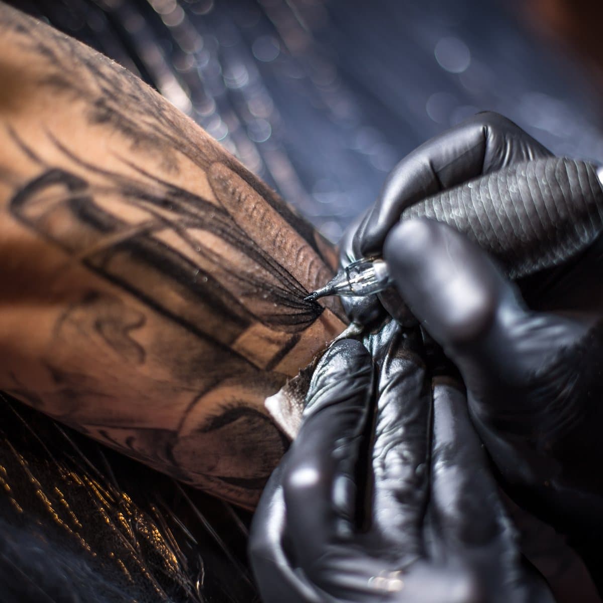 A tattoo artist working on a client’s arm, machine in hand.