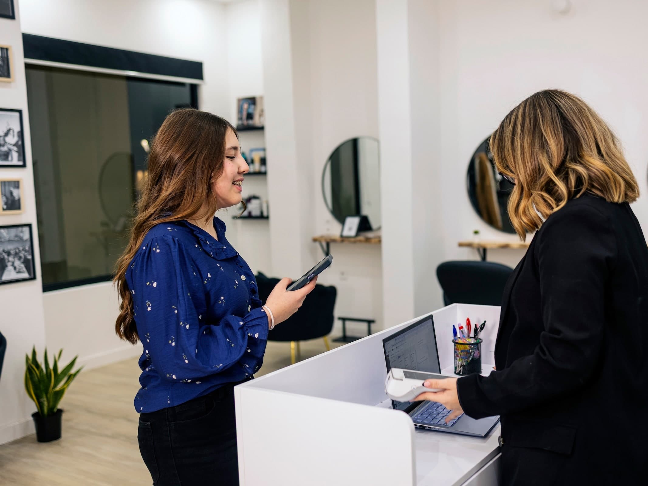 A client at a salon reception desk while a receptionist takes payment on a card terminal.